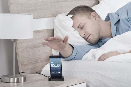 man pressing snooze button while sleeping
